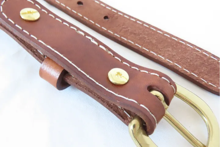 a close up of a leather belt showing chicago screws, adjustment holes, and a solid brass buckle.